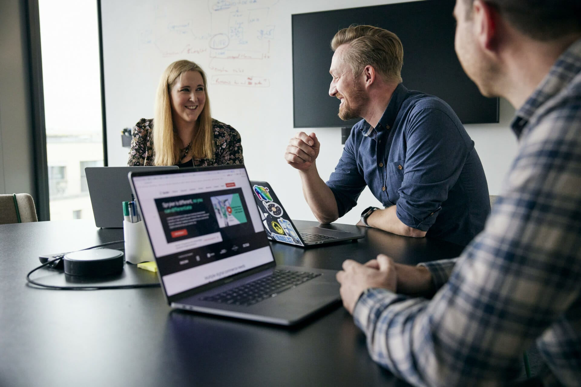 Three people are engaged in a meeting around a table with laptops. Two men and one woman, discussing their company's impressive positioning in the Gartner Magic Quadrant, are smiling and talking in a modern office setting.