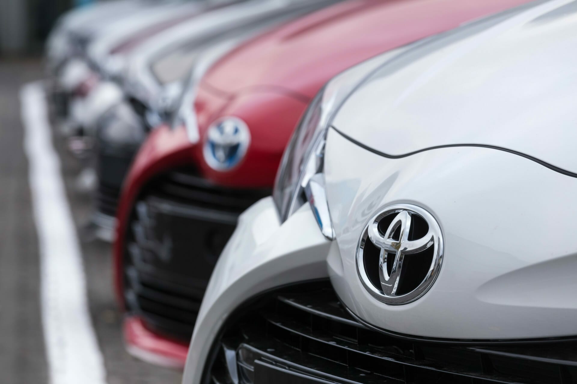 Close-up of the front grilles and emblems of several parked Toyota cars in different colors, including white, red, and gray, showcased at the automotiveIT Kongress.