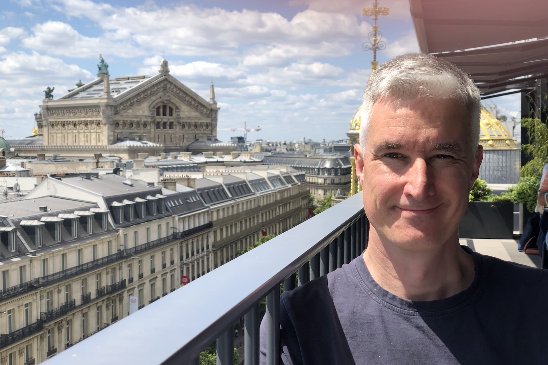 A man with short gray hair, identified as the Spryker CMO, stands on a balcony overlooking a cityscape with historic buildings and a blue sky with scattered clouds.