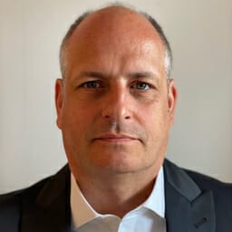 Bald man in a dark suit jacket and white shirt, looking straight at the camera against a plain background, embodying the professionalism of someone on a customer advisory board.