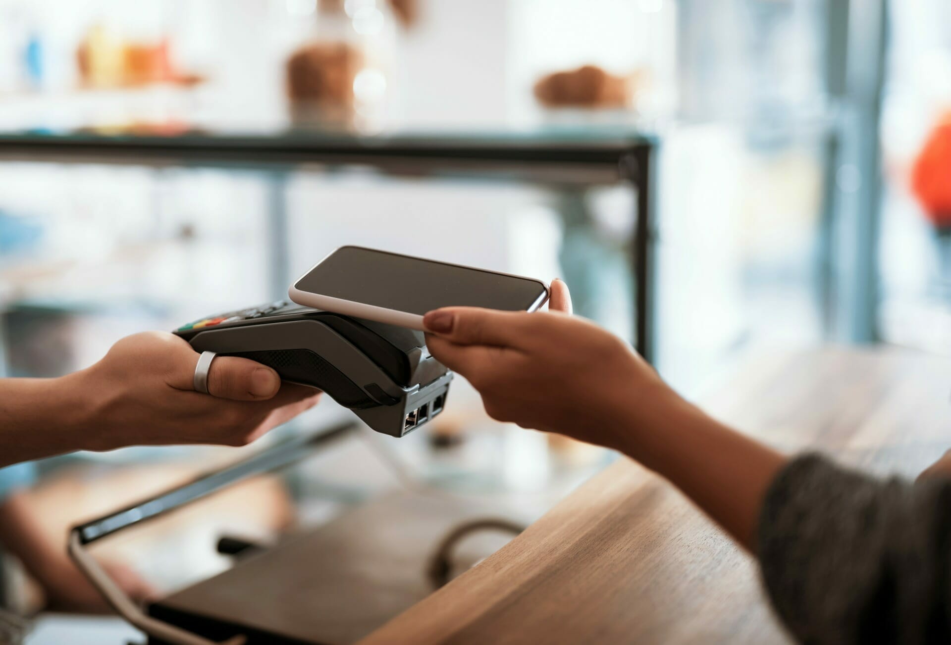A person holds a smartphone over a payment terminal, completing a seamless contactless mobile payment transaction in a store, exemplifying the convenience of headless commerce.