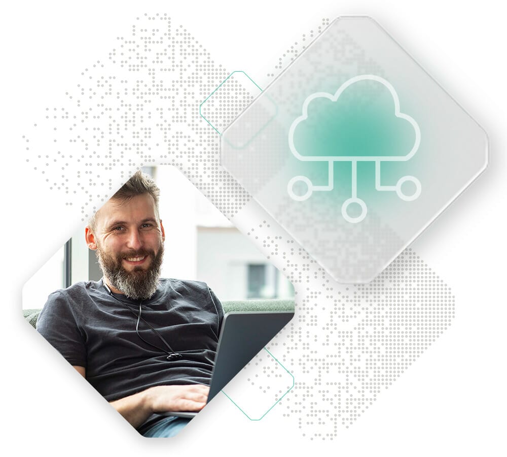A bearded man is seated comfortably on a couch, using a laptop. He appears to be working or browsing, with an IoT commerce graphic overlay nearby.