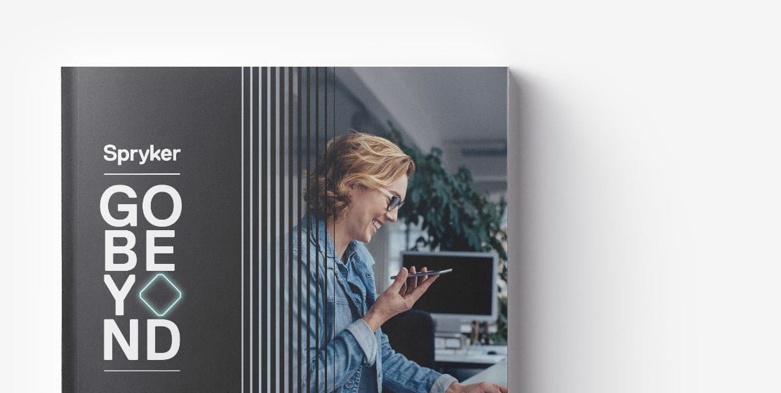 A person with shoulder-length hair and glasses is talking on the phone while using a laptop. The text on the cover of the magazine reads "Spryker Go Beyond Intrapreneurs in eCommerce.