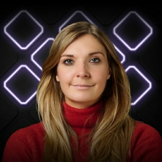 A woman with long blonde hair wearing a red turtleneck sweater stands in front of a dark background with glowing square patterns, capturing the vibrant energy reminiscent of Spryker EXCITE 2022.