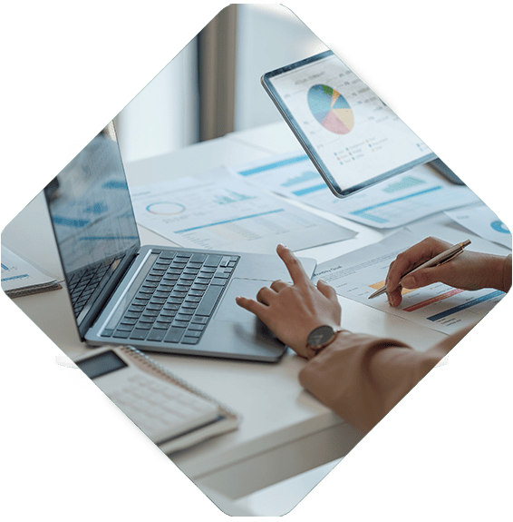 Person working at a desk with a laptop, tablet, and various charts and graphs on paper, seamlessly managing composable commerce strategies.