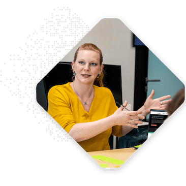 A person with red hair wearing a yellow shirt sits at a table, gesturing with hands, during a discussion on digital transformation.