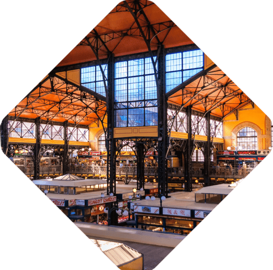 An interior view of a large, industrial-style market hall with multiple levels, bright lighting, and various vendor stalls, where expert guides offer insights into local products.