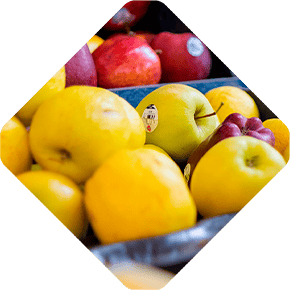 Apples and lemons are displayed in a diamond-shaped frame, set against a metro-inspired backdrop with vibrant yellow, green, and red hues.